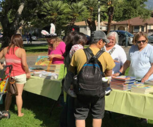 Table of books with people checking out all the books.