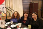 Three ladies sitting a table with big smiles.